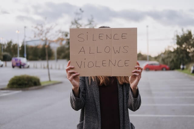une femme avec pancarte écrit silence allows violence